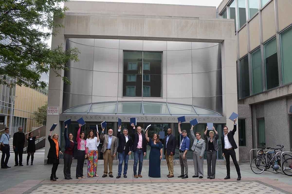 Alums pose in front of Annenberg School with their dissertations