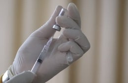 white gloved hand filling up a syringe from a vial; Photo by Mufid Majnun on Unsplash