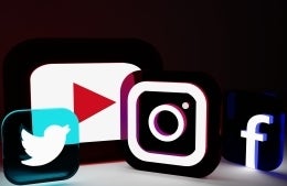 Lit-up boxes showing social media icons against black background. From L to R: Twitter, YouTube, Instagram, and Facebook.